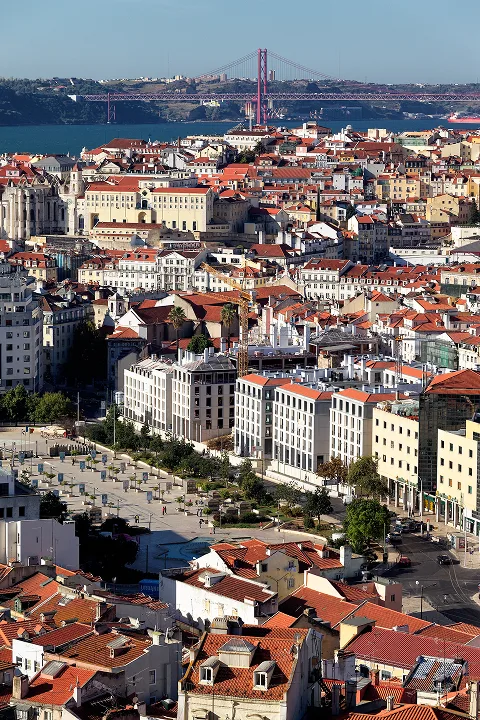 Vibrant view of downtown Lisbon with the 25 de Abril Bridge in the background and a clear blue sky.