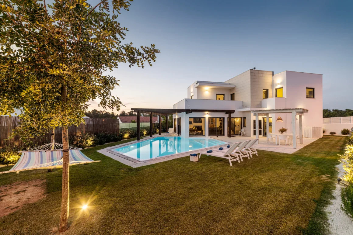 Sunset view of a modern house with garden, pool, and lounge area.
