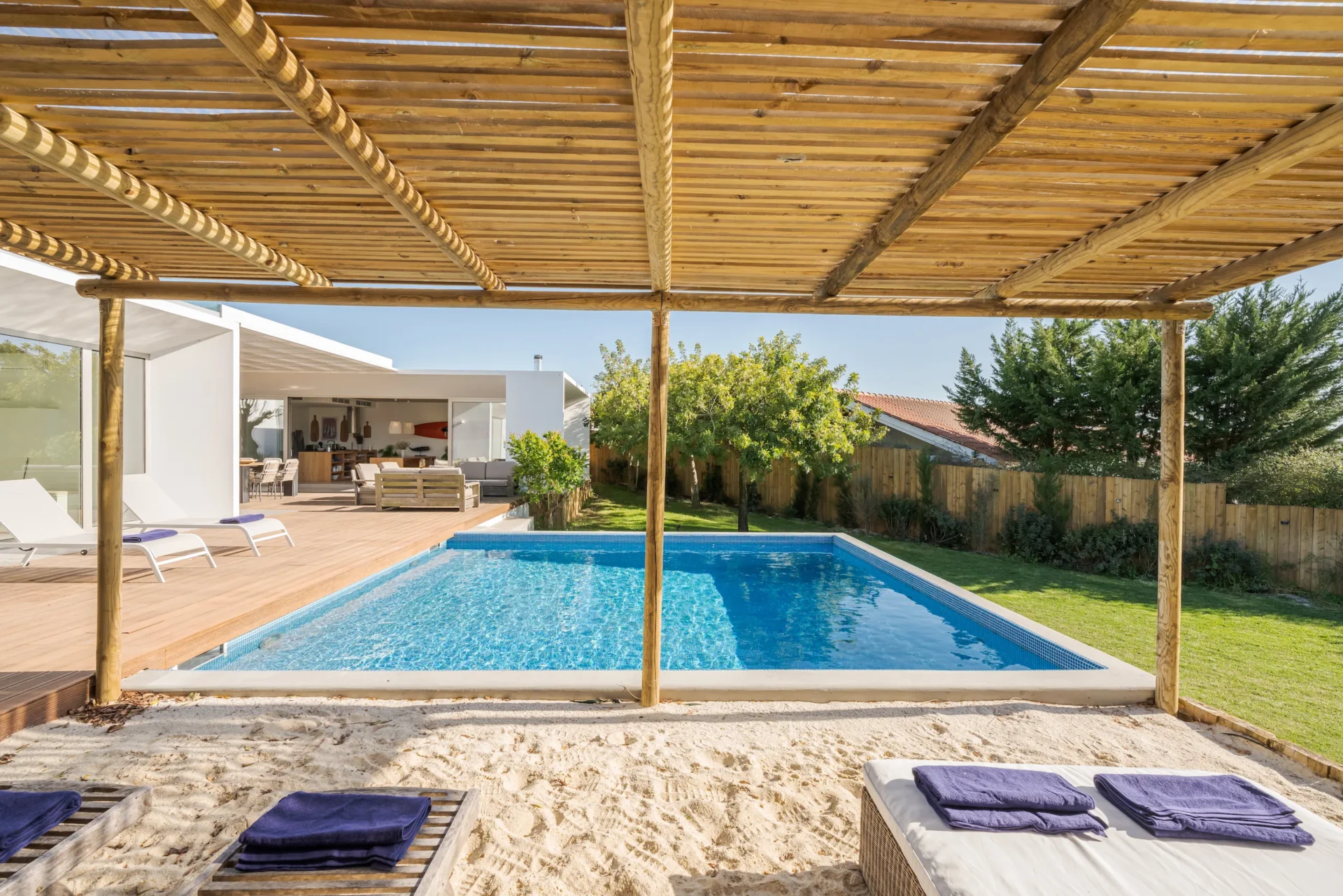 Modern villa with pool, wooden deck, lounge area, and private garden.