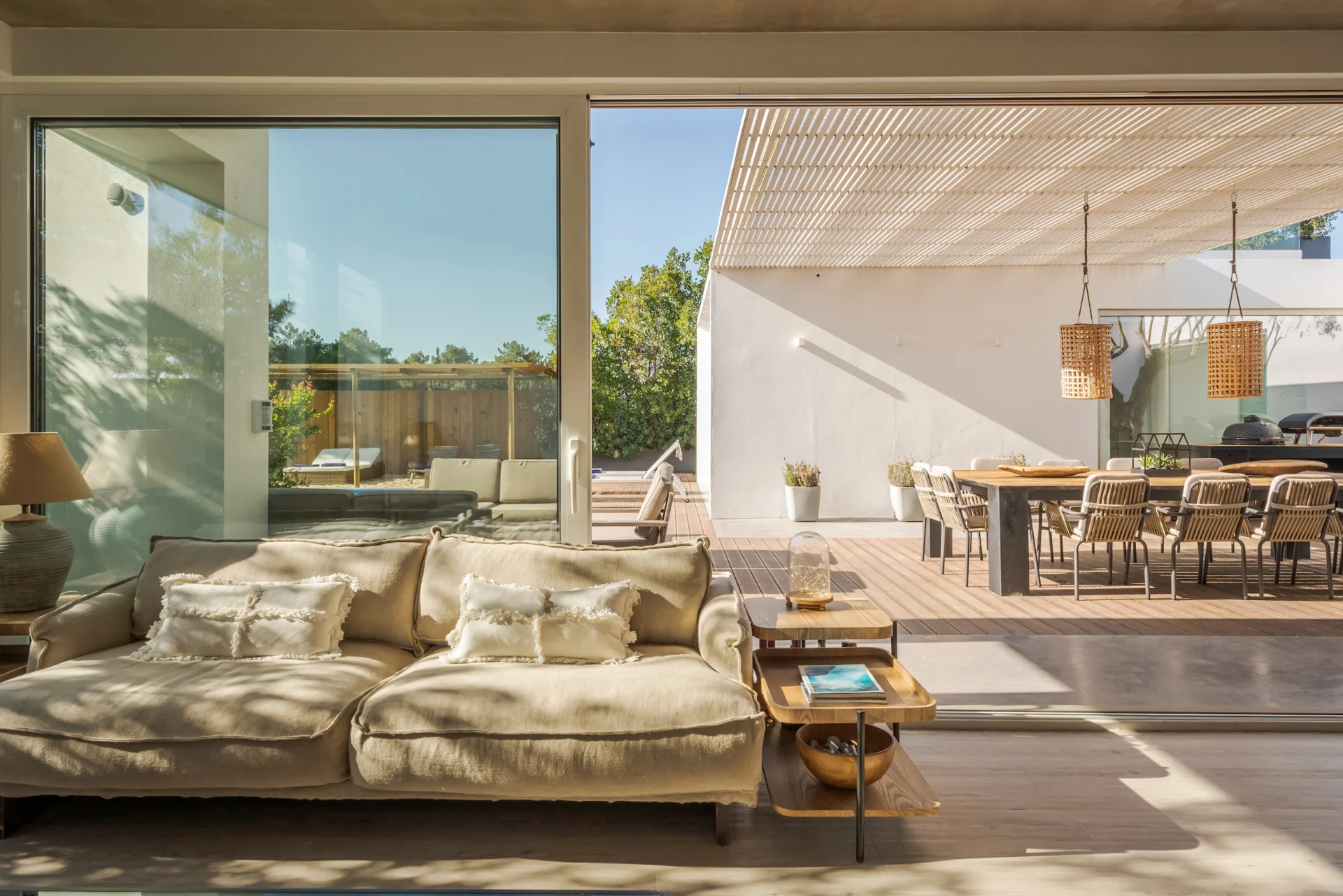 Modern villa with indoor living area opening to outdoor dining under a pergola.